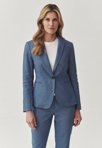 Modrý texturovaný blazer s přiléhavým střihem, s jedním knoflíkem a ostrými klopami. Nosit na bílou košili, v kombinaci s odpovídajícími kalhotami.
