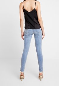 Camisole en satin noir avec des bretelles fines, associée à un jean skinny bleu clair. L'ensemble présente un dos en V et des talons beiges à lanières.
