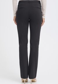 Černé kalhoty na míru s rovným střihem nohavic, mají dvě zadní kapsy, hladkou tkaninu a pas ve střední výšce.