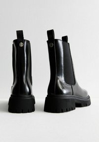 Czarne botki Chelsea mają błyszczące wykończenie, elastyczne boczne panele, pętelkę oraz grubą, bieżnikowaną gumową podeszwę dla lepszej stabilności.