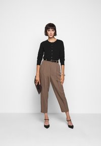Cardigan nero a maglia con bottoni, pantaloni alti marroni, cintura nera, clutch nera e scarpe con tacco. Tessuto morbido e vestibilità su misura.