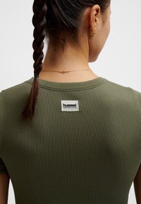 Olijfgroene geribbelde T-shirt met een ronde hals en een Hummel Performance-label aan de achterkant. Glad materiaal met korte mouwen.