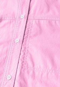 Camicia rosa a maniche corte con una texture liscia, dotata di bottoni bianchi, una tasca applicata e cuciture ordinate lungo le giunture.