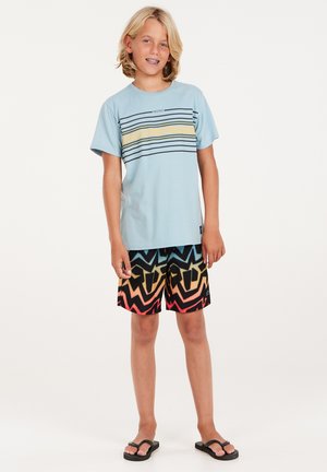 Helles blaues T-Shirt mit horizontalen Streifen in Gelb und Marineblau; schwarze Badehose mit multicolored Zickzack-Muster; schwarze Flip-Flops.