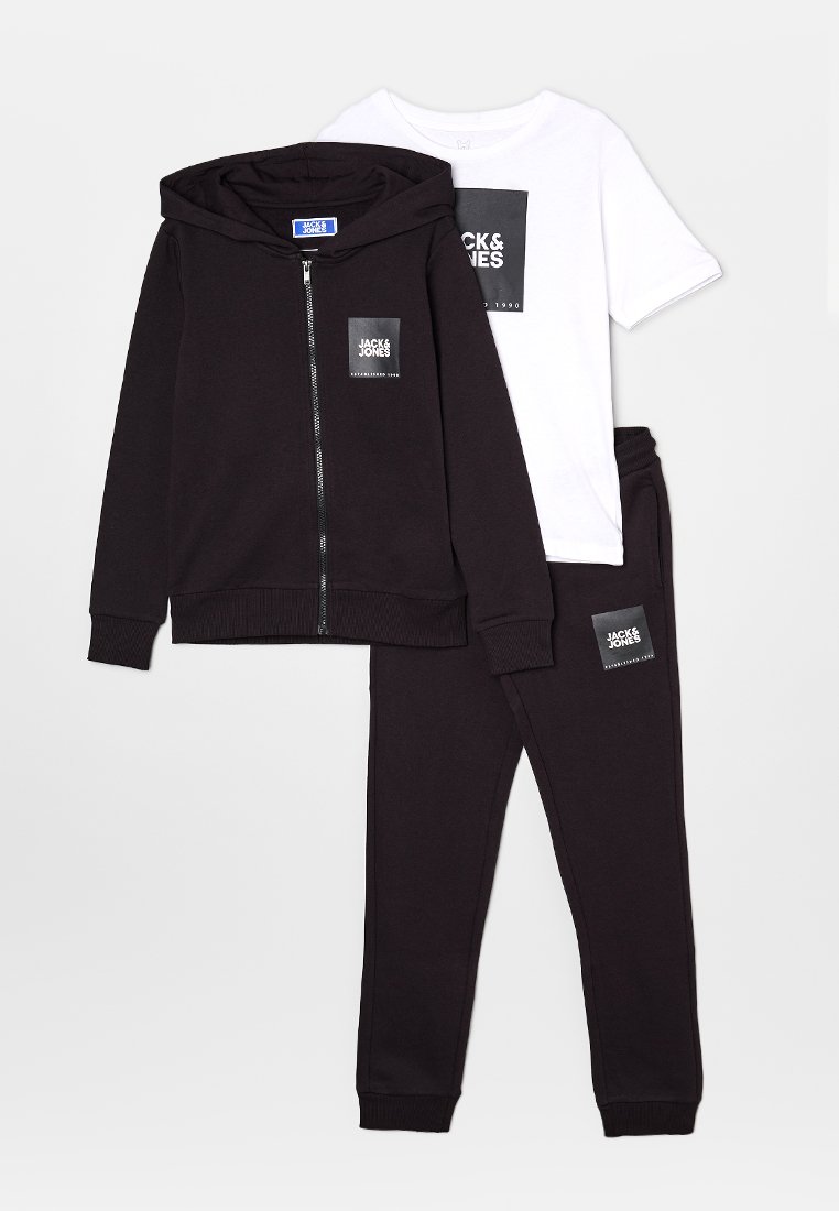 Sudadera negra con cremallera, pantalones jogger negros y camiseta blanca de manga corta con el logo "Jack & Jones" en el pecho y la pierna.