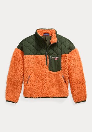Dos modelos llevan chaquetas de forro polar Polo Sport en naranja y verde, uno con pantalones beige y gafas de sol, el otro con vaqueros azules y un gorro de punto.