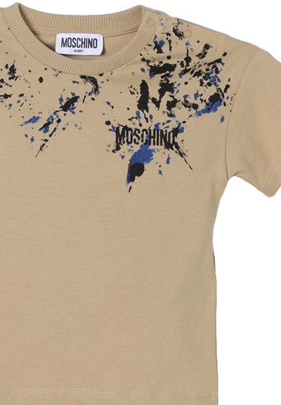 T-shirt in cotone beige con maniche corte, caratterizzato da design di vernice splatter nera e blu e logo "MOSCHINO" stampato in nero.