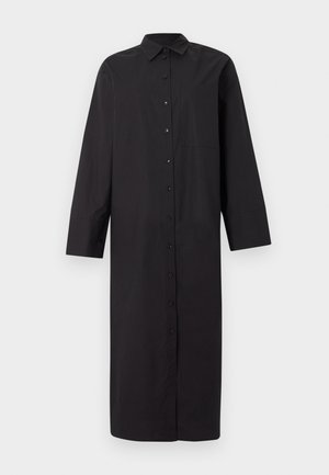 Hosszú fekete, gombos ingruha hosszú ujjakkal, gallérral és elülső zsebbel, egyszerű világosszürke háttéren kiállítva.