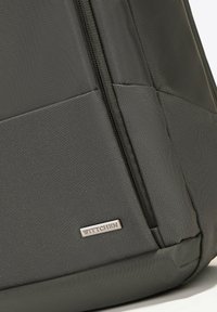 Sac en tissu gris avec une surface texturée, fermeture éclair noire et une plaque en métal portant l'inscription "WITTCHEN" sur le bas à l'avant.