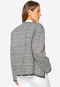 Strukturierte Tweedjacke in Marineblau und Creme mit lockerer Passform, runder Halslinie und kontrastierendem Besatz entlang der Kanten.