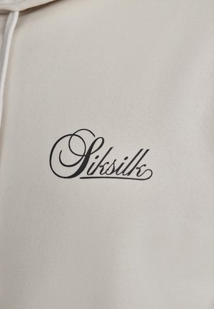 Crème-kleurige hoodie met een zwart geborduurd logo "Siksilk" met gestileerde letters op de borst. Zachte, gestructureerde stof.