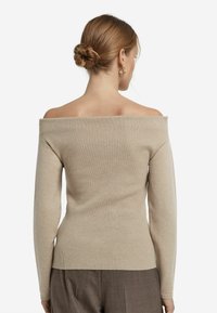 Beżowy sweter dzianinowy typu off-the-shoulder z długimi rękawami, prążkowaną fakturą i dopasowanym krojem, zestawiony z brązowymi spodniami.