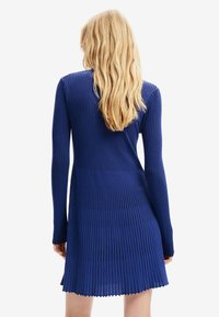 Abito in maglia a coste blu con maniche lunghe, silhouette aderente e orlo svasato. Il tessuto testurizzato con linee verticali crea un aspetto strutturato.