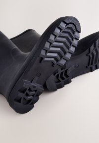 Schwarze Gummiregenstiefel mit einer strukturierten Zickzacksohle und einem glatten Schaft, ausgestattet mit einer abgerundeten Spitze und verstärkter Ferse.