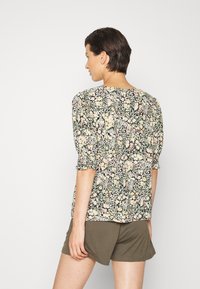 Blusa floral em preto, com tecido suave, mangas curtas bufantes e decote redondo, apresentando um padrão de flores multicoloridas por toda a peça.