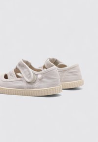 Baskets en toile beige clair avec une semelle en caoutchouc flexible, dotées de sangles croisées, d'un bout rond et d'une semelle extérieure texturée et adhérente.