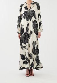 Robe longue fleurie noire et blanche avec un col montant, un détail œillet, et des manches bouffantes ; tissu lisse avec de grands motifs de feuilles.