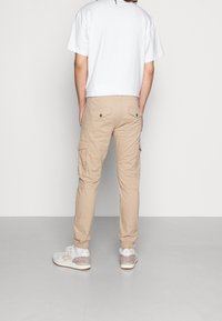 Beige cargobroek met zijzakken en elastische boorden, gemaakt van lichte stof, gecombineerd met een eenvoudig wit T-shirt en sportschoenen.