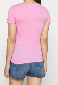 Różowa koszulka z krótkim rękawem, lekkotkaninowa, okrągły dekolt, gładka tekstura, lekko dopasowany krój, zestawiona z dżinsowymi szortami.