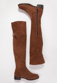 Brązowe zamszowe kozaki za kolano z zaokrąglonym czubkiem, zamkiem błyskawicznym z boku i ozdobą w postaci klamry, z niskim, warstwowym obcasem i gładką fakturą.