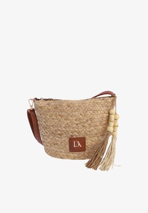 Bolso bandolera de paja trenzada con correa de cuero, parche de logo marrón y dos borlas con cuentas de madera colgando a un lado.