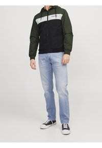 Giacca con cappuccio con corpo nero, maniche verdi e yoke anteriore bianco. Chiusura frontale con zip, polsini elastici e logo ricamato sul petto.