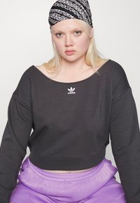 Sweatshirt preto cropped com decote largo e logótipo no peito, combinado com calças soltas de cor roxa clara. Faixa de cabelo preta estampada.