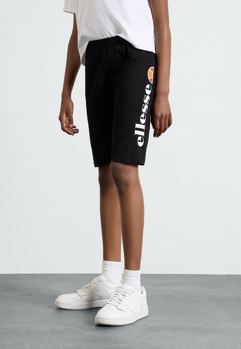 Čierne šortky s elastickým pásom, na ktorých je biele logo "ellesse" a oranžová a žltá embléma. V kombinácii s bielymi teniskami a ponožkami.