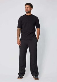 T-shirt noir à manches courtes associé à un pantalon noir ample. La tenue présente une texture lisse et un design simple. Une paire de chaussures noires complète le look.