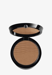 Rund bronzepudderkompakt med en glansfull svart finish. Har en teksturert brun pudderoverflate med bølgemønstre. Sølvlogo på toppen.
