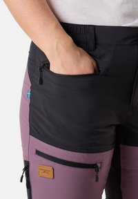 Pantaloni da esterno neri e viola con design aderente. Presentano molteplici tasche con zip e un'etichetta in pelle. Texture liscia.
