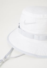 Weißer Bucket Hat aus texturiertem Stoff, graues verstellbares Band und ein dezentes graues Nike-Logo auf der Vorderseite. Mit breiter Krempe.
