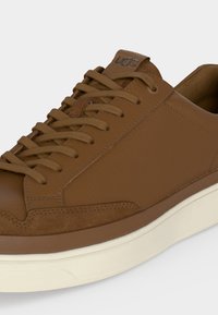 Baskets en cuir marron avec lacets assortis, détails en daim, logo UGG sur la languette et semelle épaisse en caoutchouc blanc.