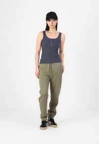 Grå ribbet tanktop med knappedetaljer, kombinert med olivengrønne joggebukser med elastisk midje og mansjetter, samt svarte joggesko.