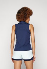 Marineblaues ärmelloses Oberteil mit hohem Kragen und strukturiertem Stoff. Verfügt über ein tailliertes Design, kombiniert mit hellblauen Shorts und marineblauen Akzenten.