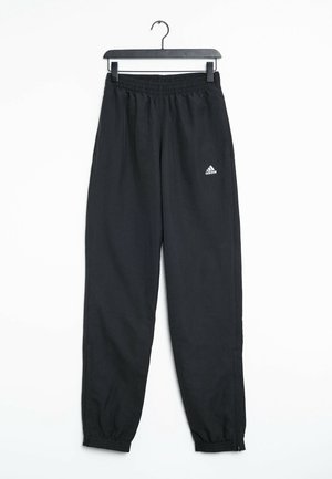 Pantalon de survêtement noir Adidas avec taille et poignets élastiques suspendu à un cintre noir sur fond blanc.