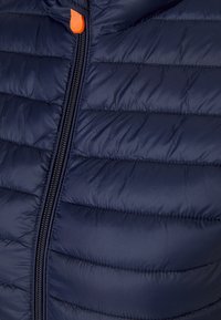Giacca puffer trapuntata blu navy con colletto alto, dotata di zip nera e linguetta arancione per una chiusura facilitata. Texture liscia.