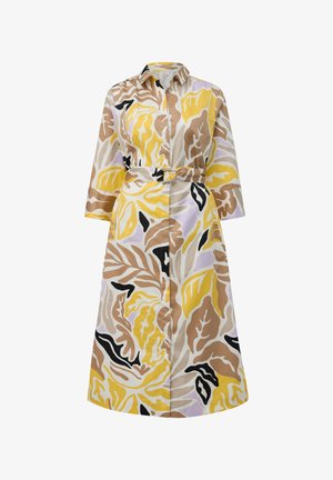 Lange shirtdress met een kraaghalslijn, een ceintuur in de taille en kleurrijke bladpatronen in geel, bruin en zwart op een lichte stof.