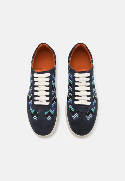 Marinblå mockaskor med flerfärgade zigzag-mönster, vita snören och orange innersulor, rund tå och vadderade sulor.