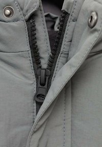 Gray jacket zipper close-up, featuring a durable black zipper fastener, snap closure, and textured fabric with visible stitching.