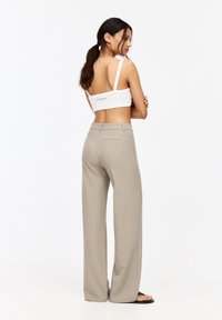 Top court blanc à fines bretelles, avec un logo dans le dos ; associé à un pantalon beige taille haute à jambe large. Texture lisse, design minimaliste.
