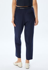 Donkerblauwe tailored broek met een rechte pijp, voorzien van een smalle zwarte riem, subtiele achterzak en een gladde textuur.