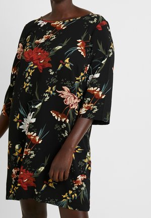 Sort kjole med stort blomsterprint i rødt, pink, gult og hvidt samt albuelange ærmer båret af en mørkhudet person.