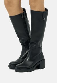 Bottes noires montantes en cuir synthétique lisse, avec une fermeture éclair sur le côté, un embout arrondi, un talon épais et un discret accent logo.