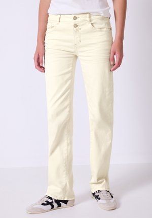 Jean droit jaune clair avec un design classique à cinq poches, fermeture à deux boutons et des détails de couture subtils. Assorti à des chaussures blanches et noires.