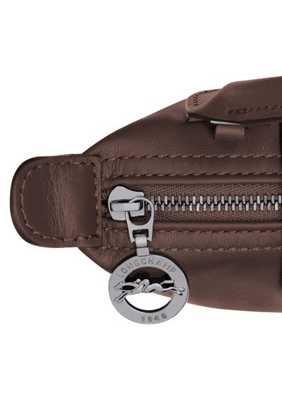 Brown leather bag zipper with silver circular Longchamp 1948 logo pull tab showing a horse and rider.