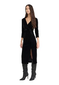 Czarna aksamitna sukienka z długimi rękawami i zapięciem w stylu kopertowym, z bocznym rozcięciem i wewnętrzną warstwą siateczkową. Połączona z błyszczącymi czarnymi botkami.