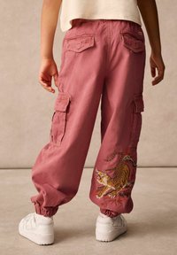 Rosa cargobyxor med elastiska muddarna, prydda med en tigermönstring och flera fickor. Matchas med vita sneakers.