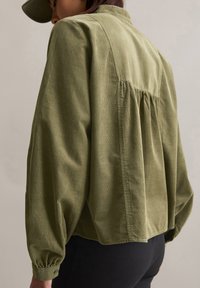 Chemise en velours côtelé vert olive à coupe décontractée, dotée d'une empiècement au dos et de détails froncés, finie par des poignets boutonnés et un ourlet arrondi.