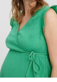 Vihreä kääntömekko, joka on valmistettu teksturoidusta kankaasta. Mekossa on V-kotelo, lyhyet hihat ja vyötäröä korostava solmivyö.